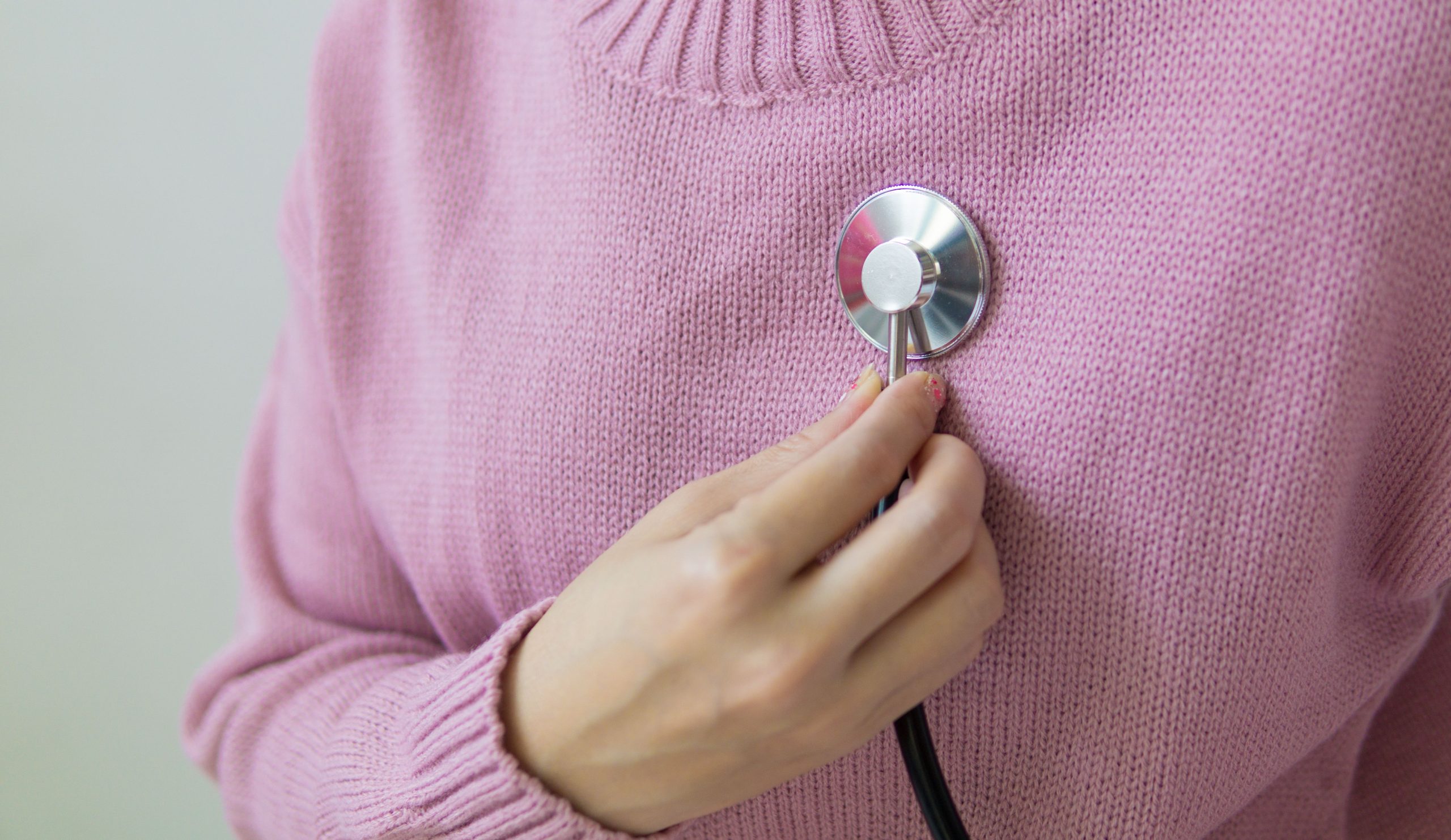Femme en pull rose ausculte sa poitrine