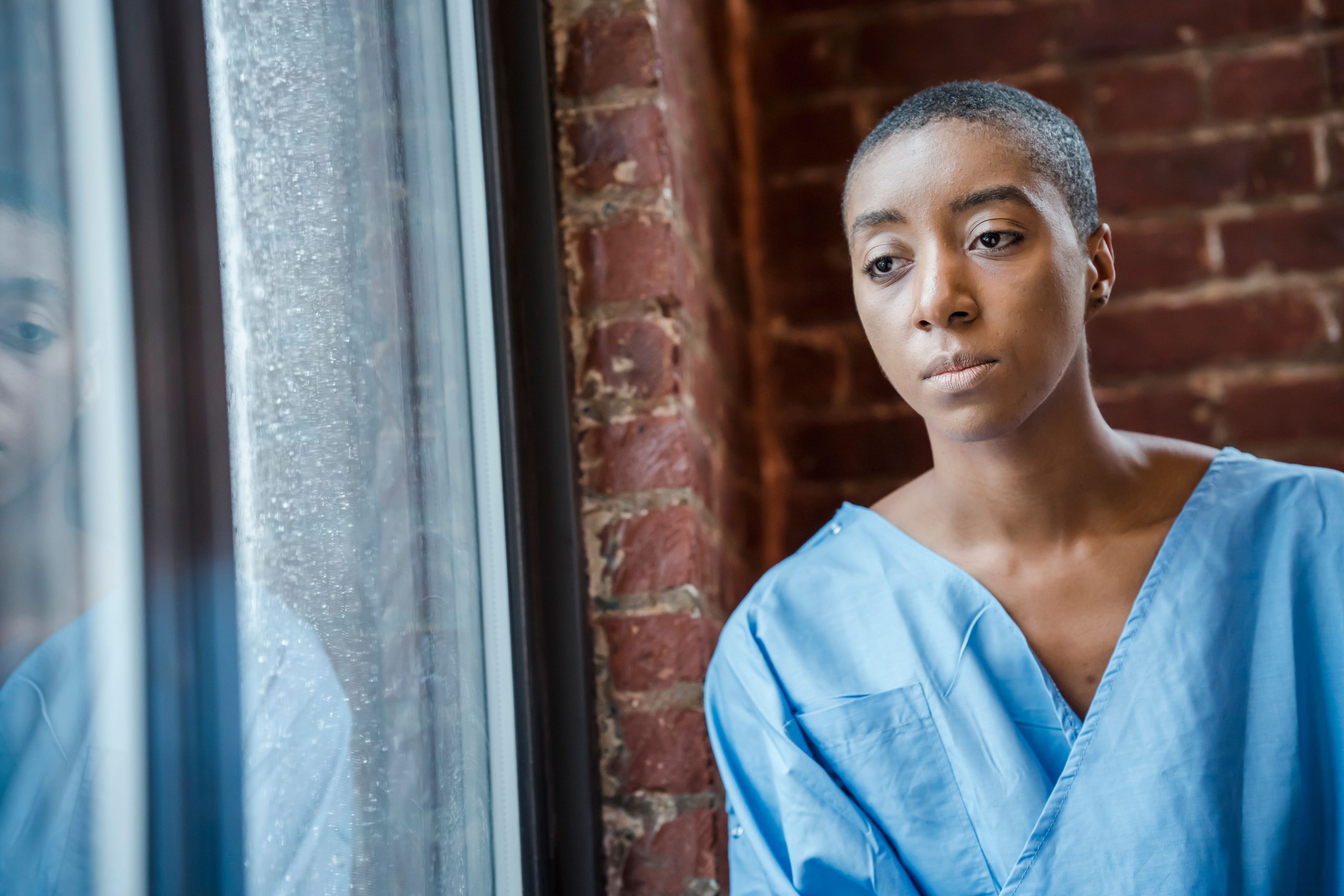 Patiente pensif en robe médicale regardant fenêtre