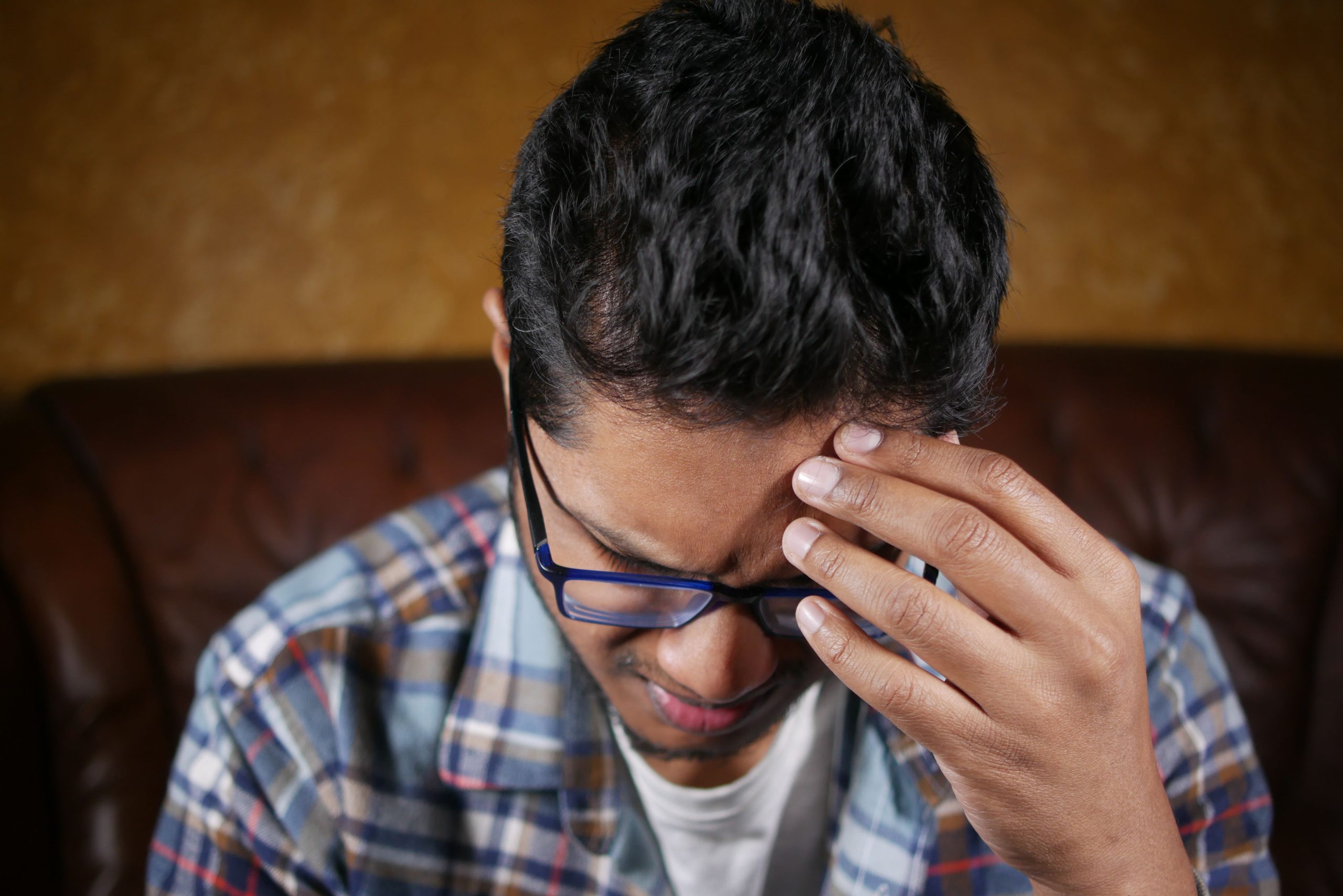 Homme avec lunettes tenant sa tête douloureuse