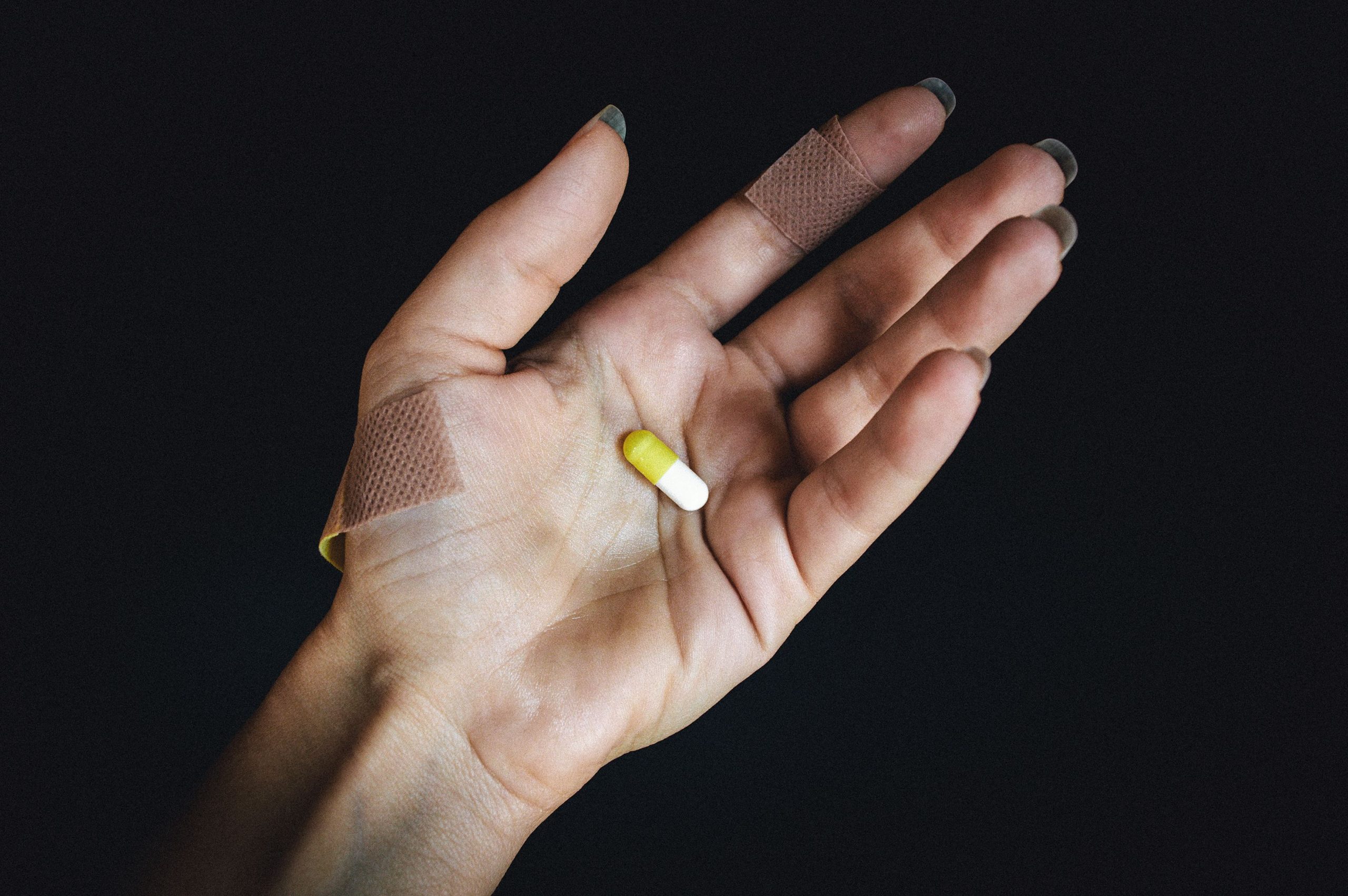 Main avec pansements tenant une capsule jaune