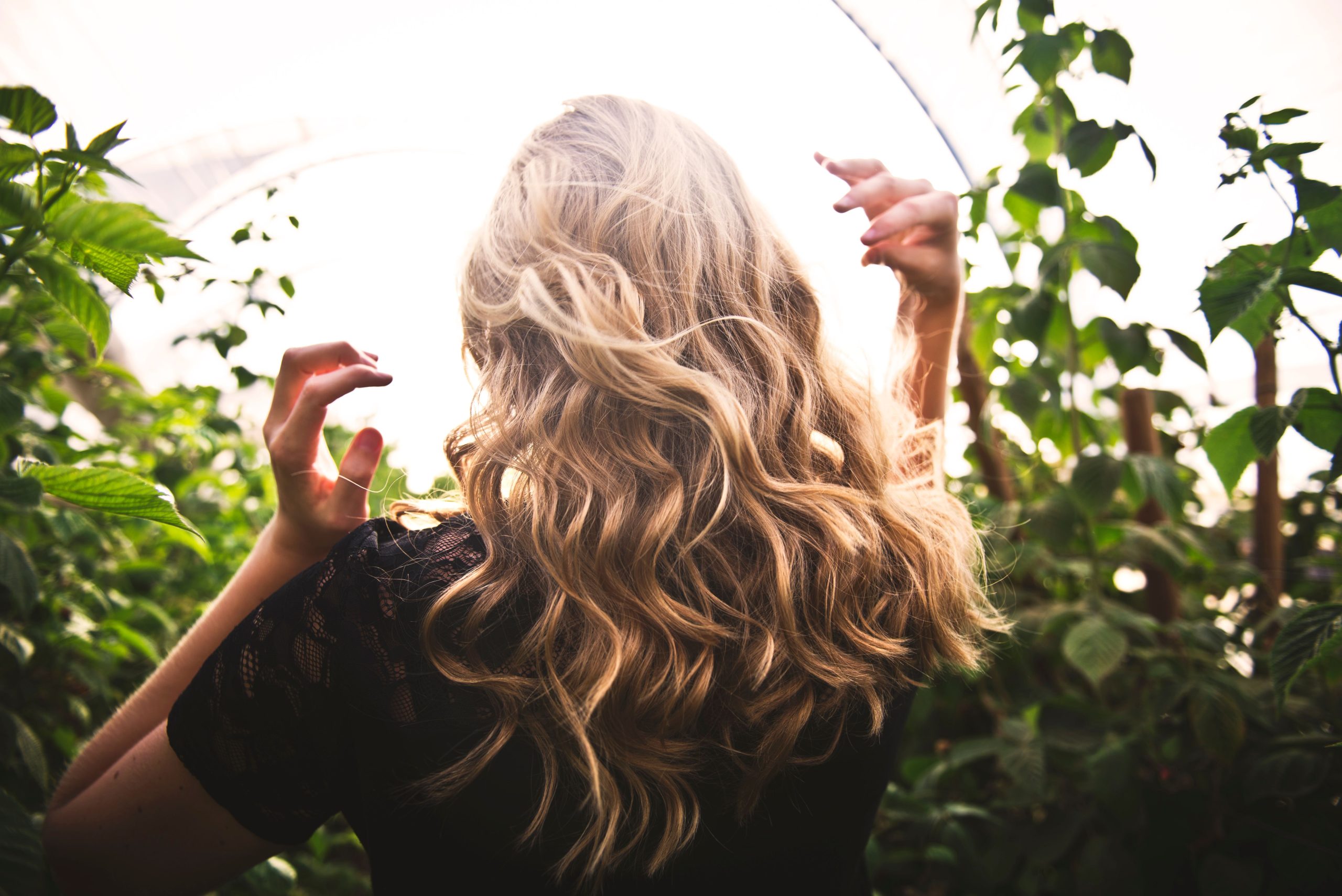 Femme blonde aux cheveux bouclés entourée de verdure