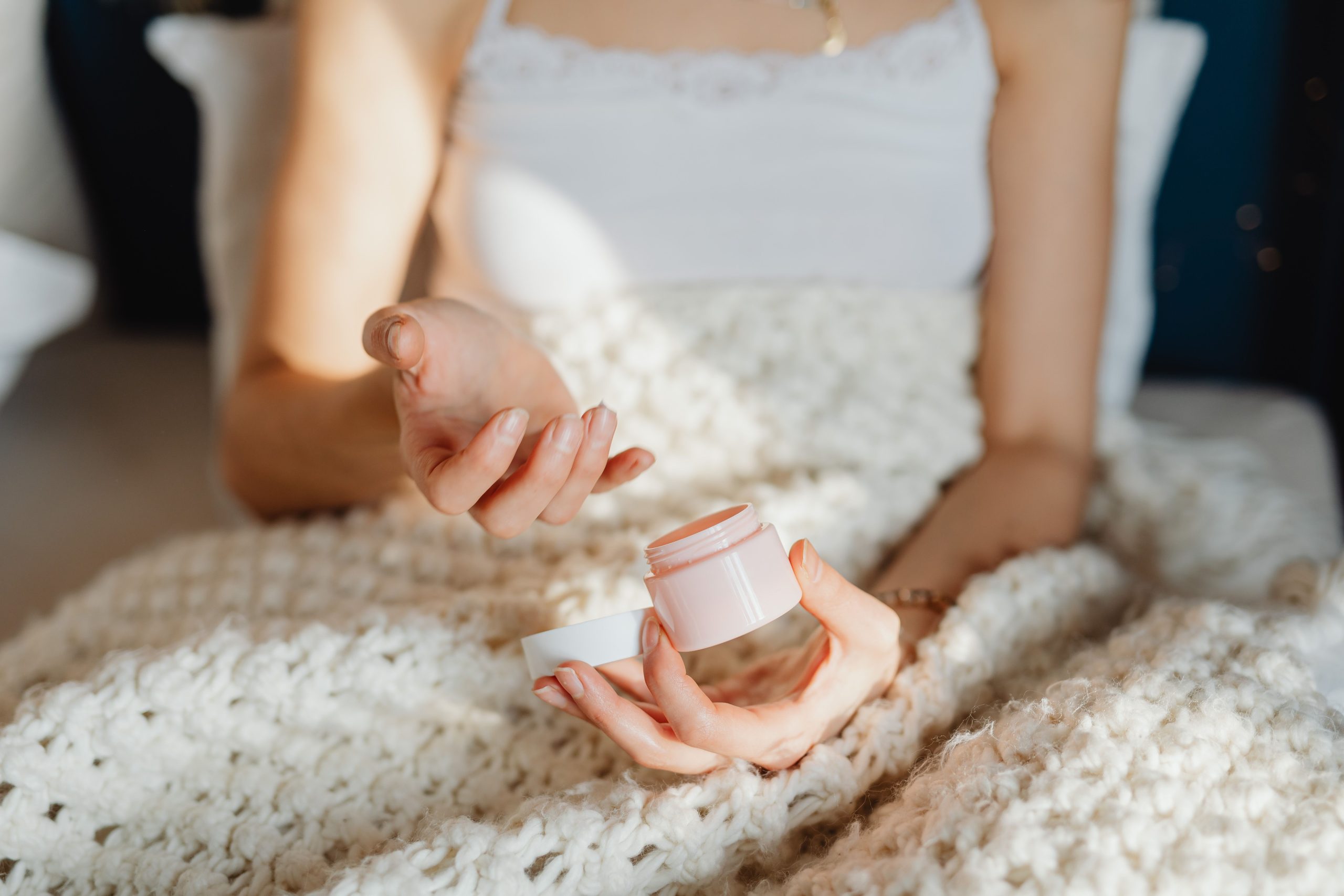 Jeune femme hydratant sa peau sous couverture
